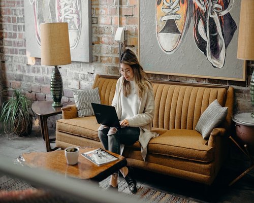 Person typing on a laptop sitting on a comfortable sofa at home